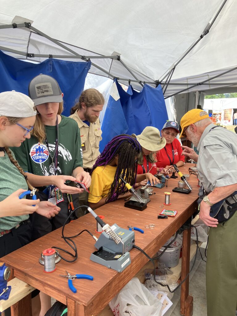 Staff and adult leaders helping Scouts learn soldering.